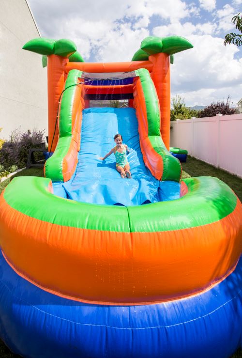 Smiling little girl playing on an inflatable slide bounce house combo outdoors 