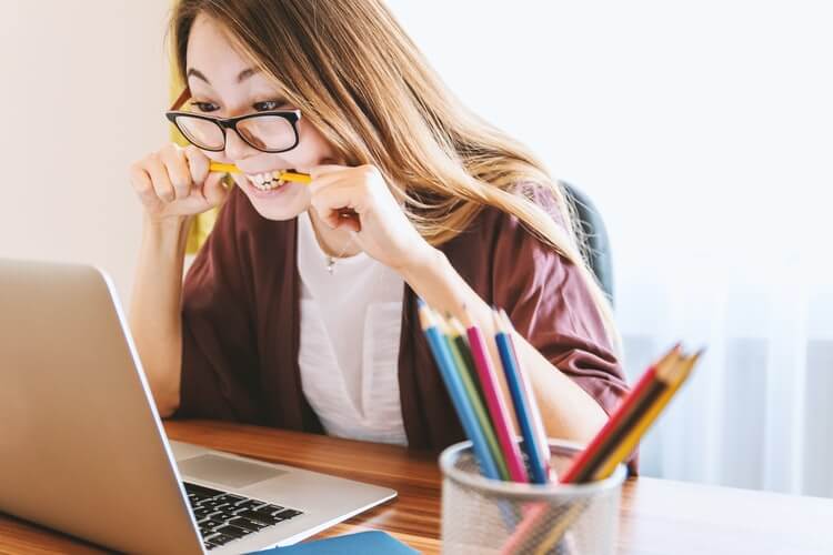 women sitting in front of computer biting pencil